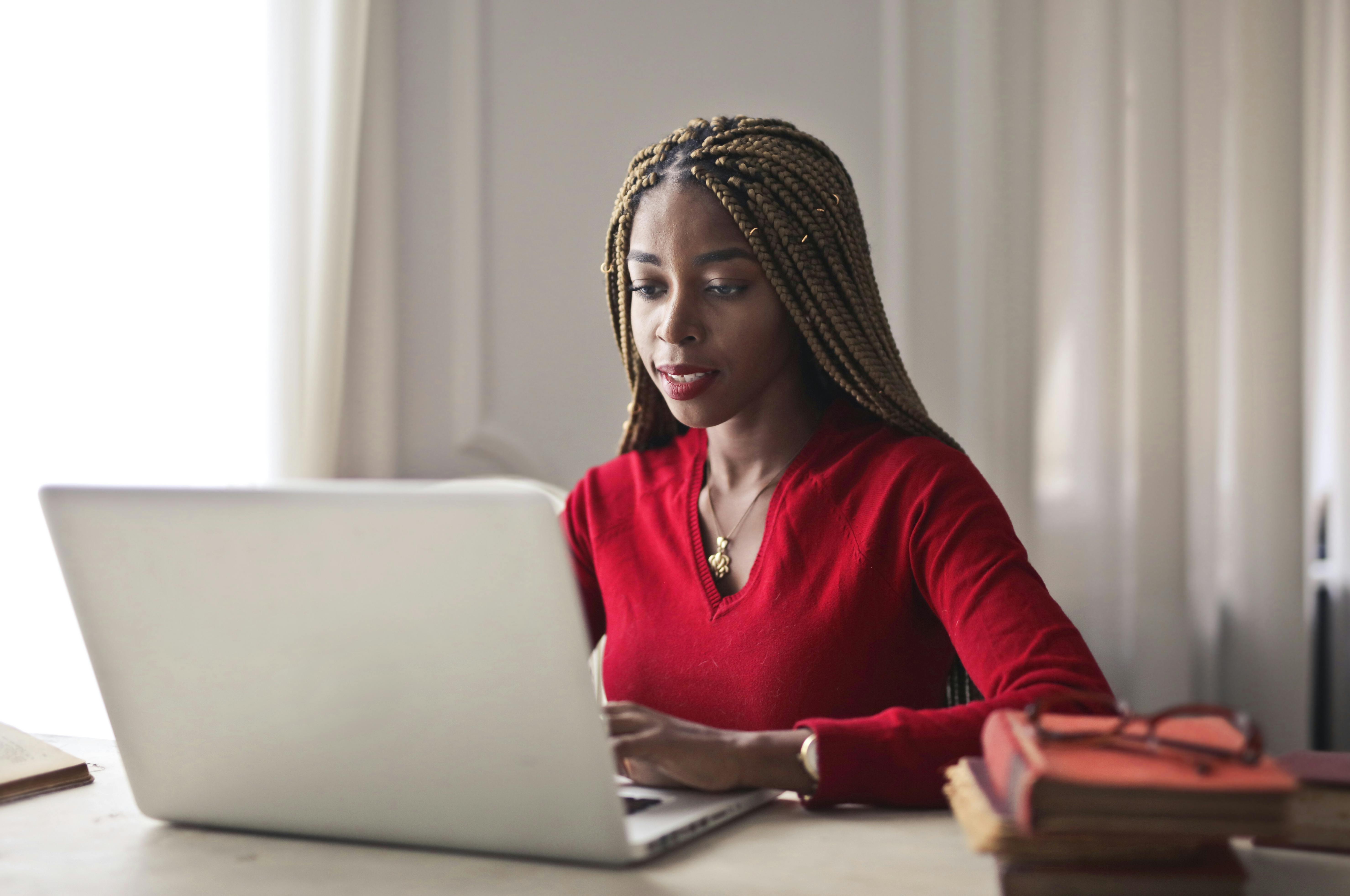 Confident woman in a red sweater working on a laptop in a bright, organized workspace.